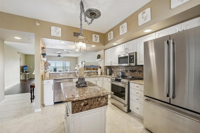 kitchen featuring kitchen peninsula, appliances with stainless steel finishes, decorative backsplash, light stone counters, and a center island