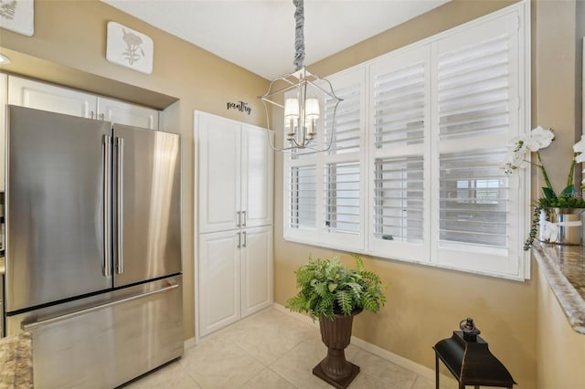 kitchen featuring stainless steel refrigerator, white cabinetry, a notable chandelier, pendant lighting, and light tile patterned floors