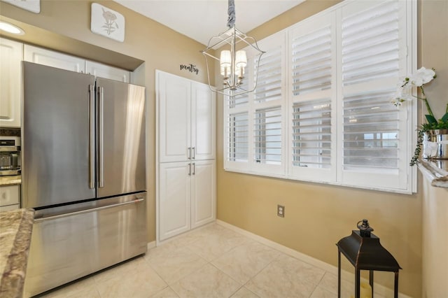 kitchen featuring stainless steel refrigerator, white cabinetry, hanging light fixtures, light stone counters, and a notable chandelier