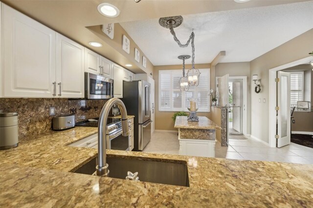 kitchen featuring appliances with stainless steel finishes, sink, white cabinetry, hanging light fixtures, and light tile patterned flooring