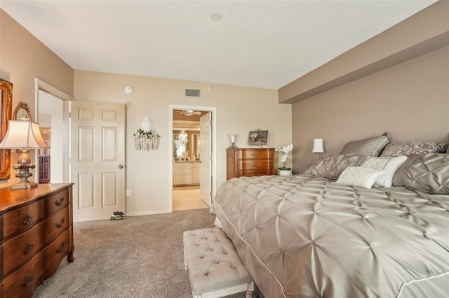 carpeted bedroom with ensuite bathroom and a textured ceiling