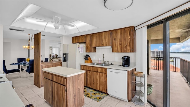 kitchen with light tile patterned flooring, white appliances, ceiling fan with notable chandelier, sink, and a kitchen island