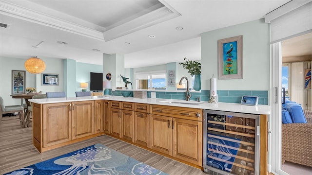 kitchen featuring sink, beverage cooler, a raised ceiling, kitchen peninsula, and decorative light fixtures