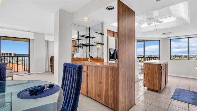 kitchen featuring fridge with ice dispenser, ceiling fan, kitchen peninsula, and light tile patterned floors