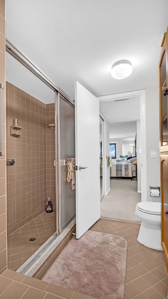 bathroom featuring tile patterned flooring, a shower with door, and toilet