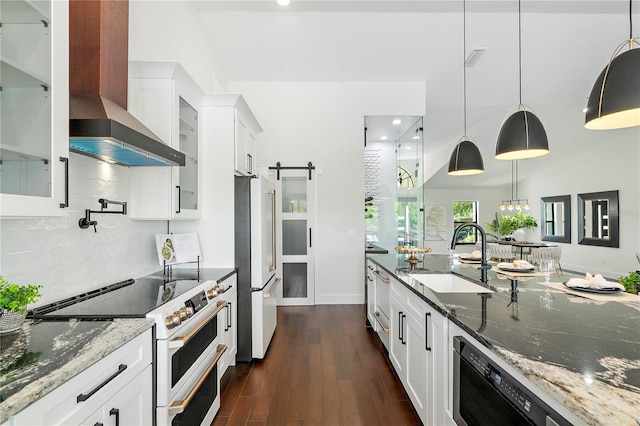 kitchen with high quality appliances, dark stone countertops, sink, a barn door, and white cabinetry