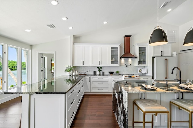 kitchen featuring wall chimney range hood, dark hardwood / wood-style flooring, white cabinetry, lofted ceiling, and dark stone countertops