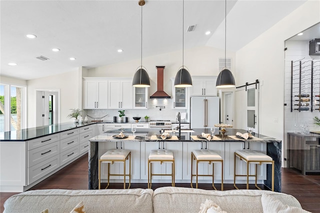 kitchen featuring high end white refrigerator, vaulted ceiling, a barn door, pendant lighting, and custom exhaust hood