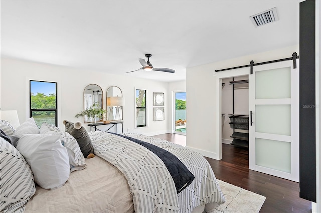 bedroom with ceiling fan, multiple windows, dark hardwood / wood-style flooring, and a barn door