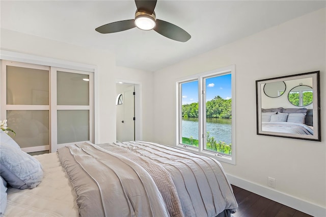 bedroom featuring a water view, ceiling fan, and dark wood-type flooring