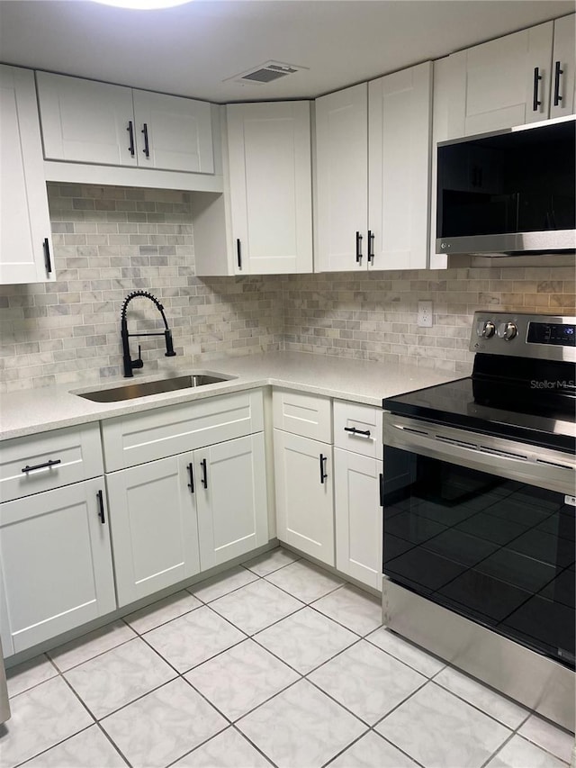 kitchen with appliances with stainless steel finishes, backsplash, sink, light tile patterned floors, and white cabinets