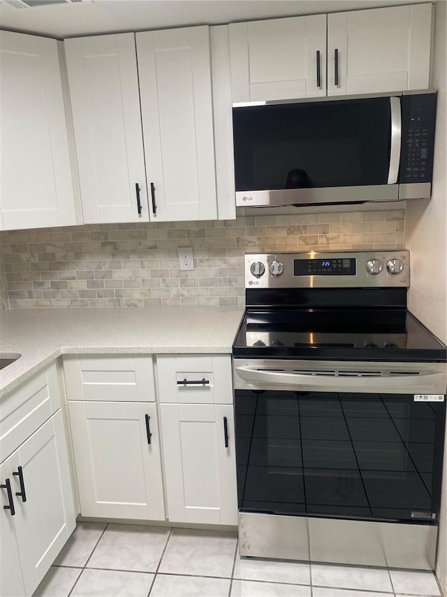 kitchen featuring tasteful backsplash, white cabinetry, light tile patterned floors, and stainless steel appliances