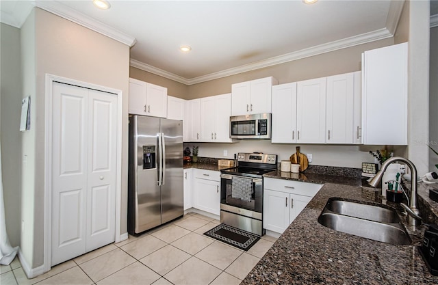 kitchen with dark stone counters, stainless steel appliances, sink, light tile patterned floors, and white cabinets