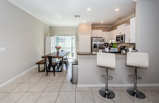 kitchen with kitchen peninsula, appliances with stainless steel finishes, light tile patterned floors, white cabinetry, and a breakfast bar area