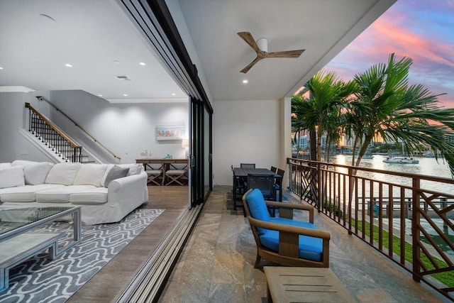 balcony at dusk with a water view, an outdoor hangout area, and ceiling fan