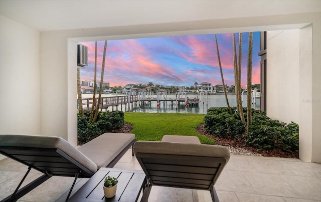 patio terrace at dusk with a boat dock, a water view, and a yard