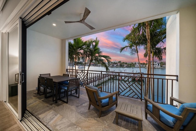 balcony at dusk with a water view and ceiling fan