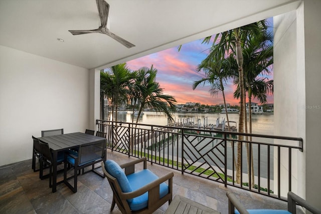 balcony at dusk featuring a water view and ceiling fan