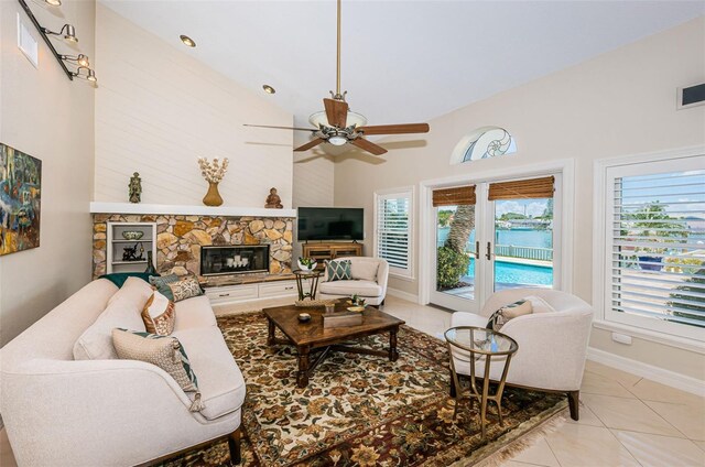 tiled living room with ceiling fan, a fireplace, a healthy amount of sunlight, and high vaulted ceiling