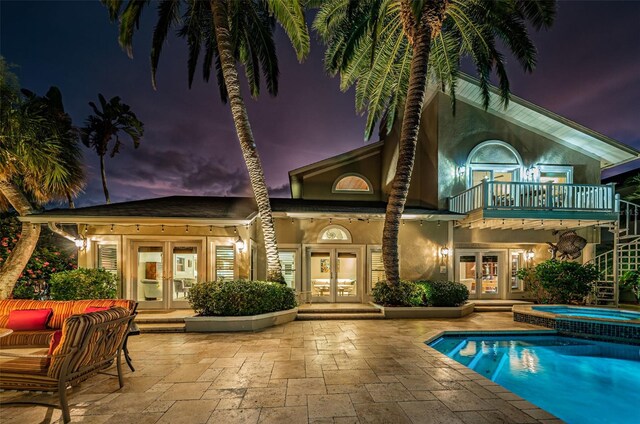 back house at dusk with a swimming pool with hot tub, a balcony, french doors, and a patio area