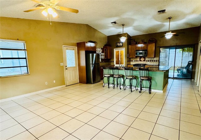 kitchen with lofted ceiling, a breakfast bar area, decorative backsplash, light tile patterned floors, and appliances with stainless steel finishes