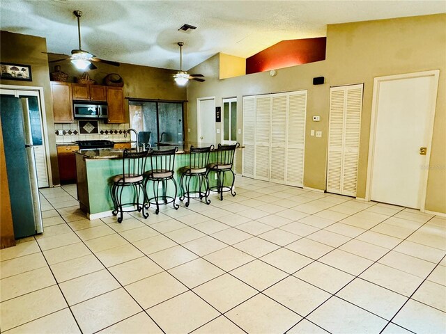 kitchen featuring lofted ceiling, a breakfast bar area, decorative backsplash, light tile patterned floors, and stainless steel appliances