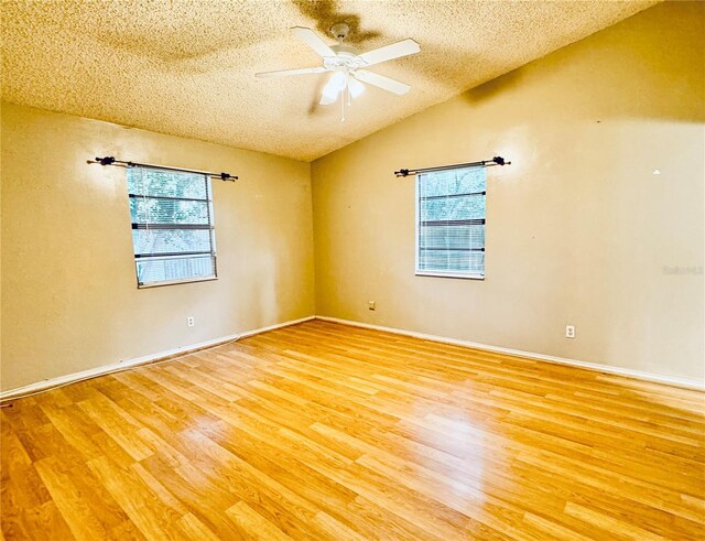 spare room featuring ceiling fan, a healthy amount of sunlight, a textured ceiling, and hardwood / wood-style flooring