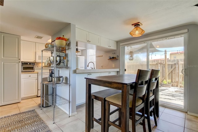 kitchen featuring kitchen peninsula, wall oven, sink, white cabinets, and light tile patterned flooring