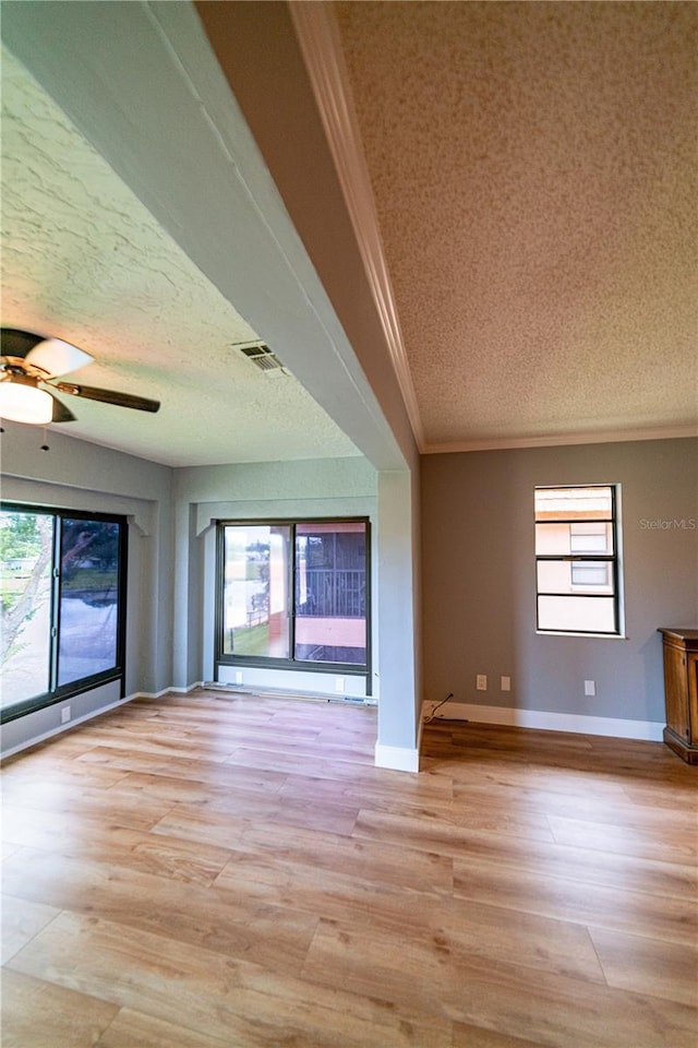 unfurnished living room with a textured ceiling, light hardwood / wood-style floors, plenty of natural light, and ornamental molding