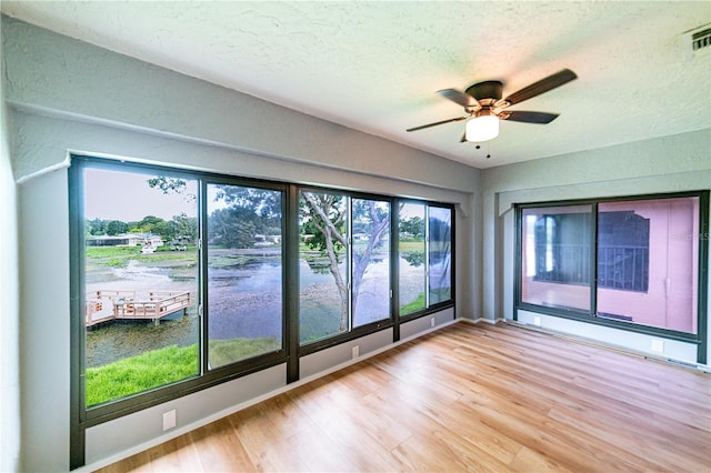 spare room featuring a textured ceiling, light wood-type flooring, ceiling fan, and a healthy amount of sunlight