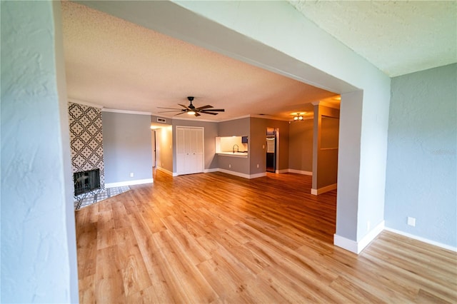 unfurnished living room featuring sink, light hardwood / wood-style flooring, ceiling fan, a textured ceiling, and a tiled fireplace