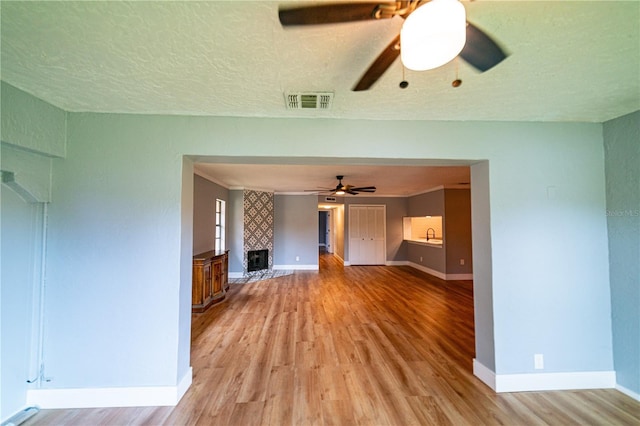 unfurnished living room with a textured ceiling, light hardwood / wood-style floors, ceiling fan, and a large fireplace