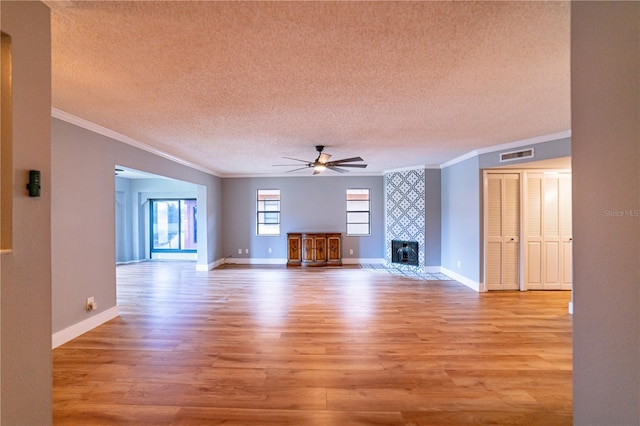 unfurnished living room featuring a tile fireplace, ceiling fan, crown molding, a textured ceiling, and light wood-type flooring