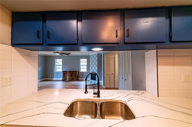 kitchen with blue cabinetry, ceiling fan, sink, light stone countertops, and hardwood / wood-style floors