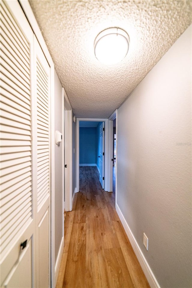 corridor with a textured ceiling and light hardwood / wood-style flooring