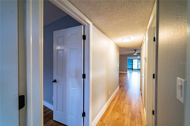 corridor featuring a textured ceiling, light hardwood / wood-style flooring, and vaulted ceiling