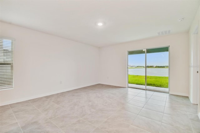 unfurnished room with a healthy amount of sunlight, a water view, and light tile patterned floors