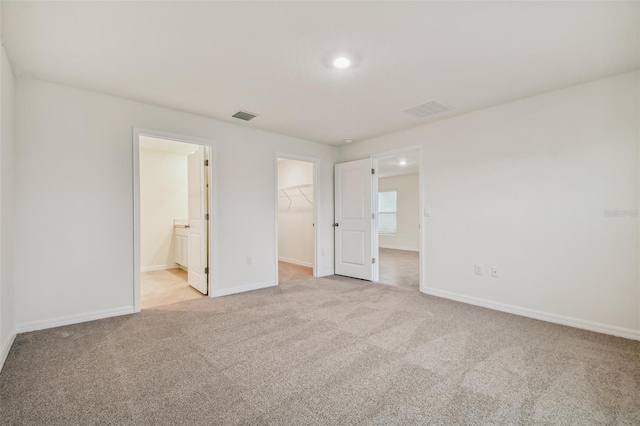 unfurnished bedroom with ensuite bathroom, light colored carpet, a walk in closet, and a closet