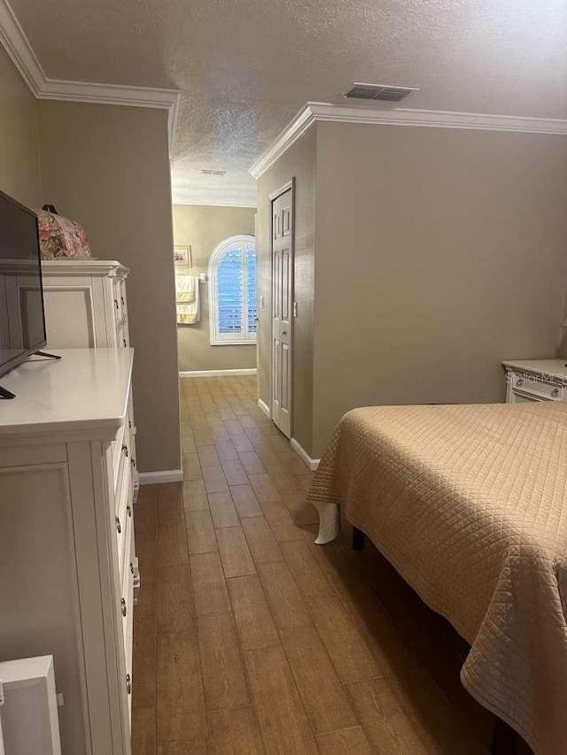 bedroom with light hardwood / wood-style flooring, a textured ceiling, and crown molding