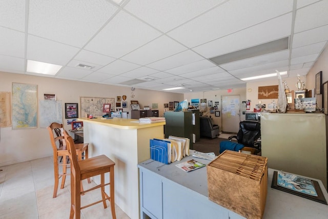 interior space with kitchen peninsula, a kitchen bar, and a drop ceiling