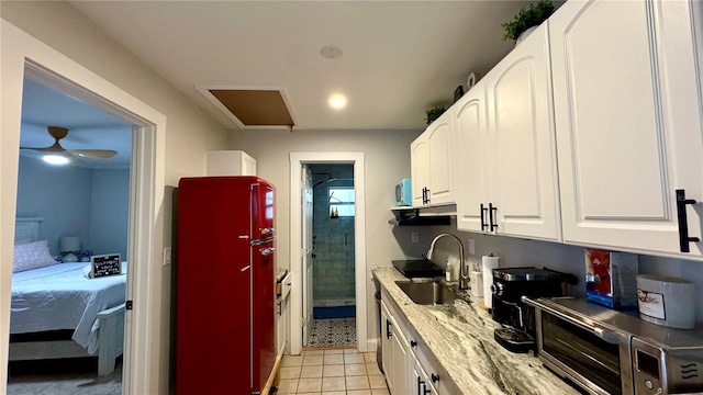 kitchen featuring light stone countertops, white cabinets, ceiling fan, light tile patterned floors, and sink