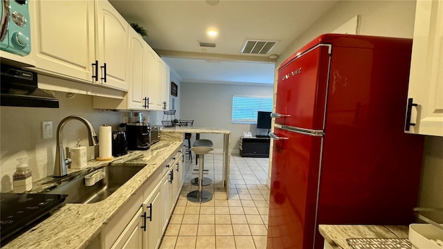 kitchen featuring light tile patterned floors, sink, light stone counters, fridge, and white cabinetry