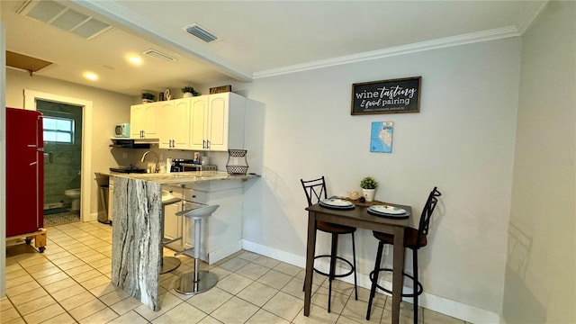 kitchen with crown molding, light tile patterned floors, white cabinetry, a kitchen bar, and kitchen peninsula