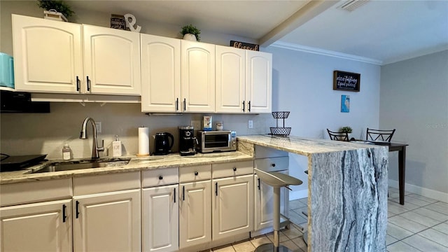 kitchen with light tile patterned floors, sink, white cabinetry, and crown molding