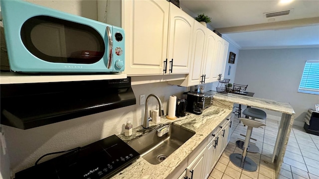 kitchen with light stone counters, light tile patterned flooring, ornamental molding, sink, and white cabinetry