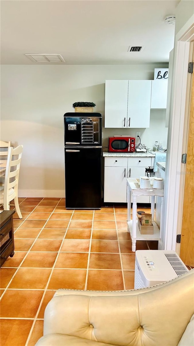 kitchen with black refrigerator, white cabinetry, and tile patterned flooring