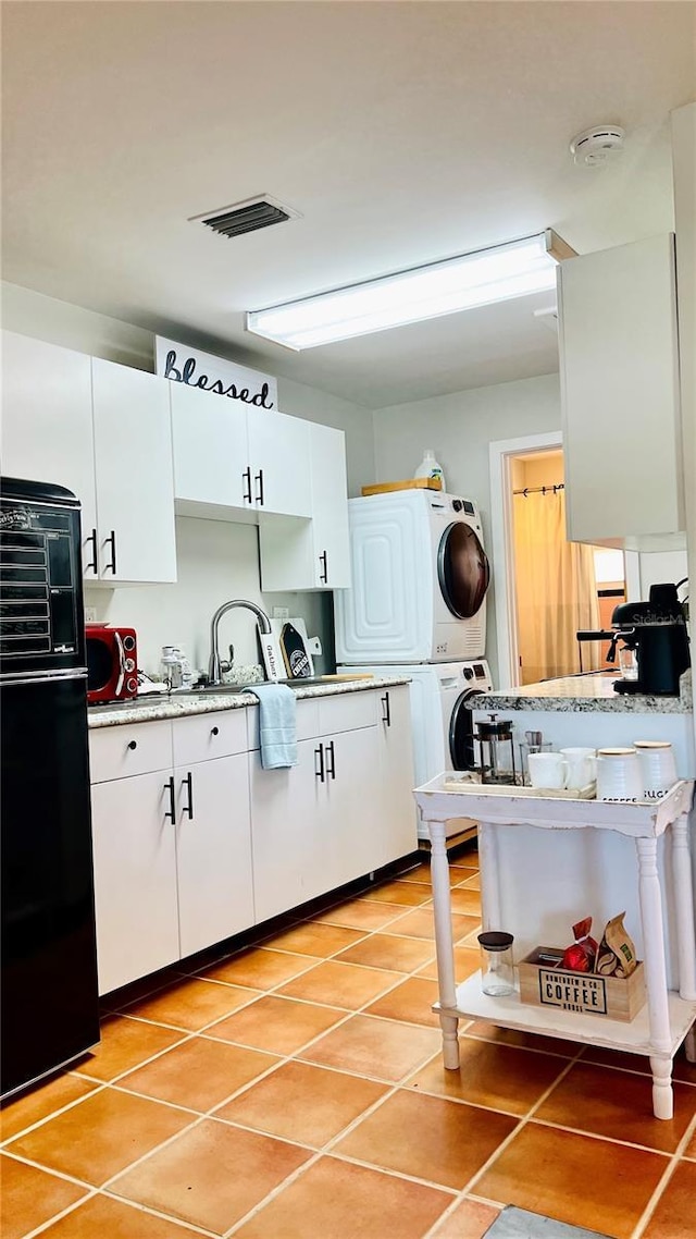 kitchen featuring light stone counters, white cabinets, stacked washer and clothes dryer, light tile patterned floors, and sink