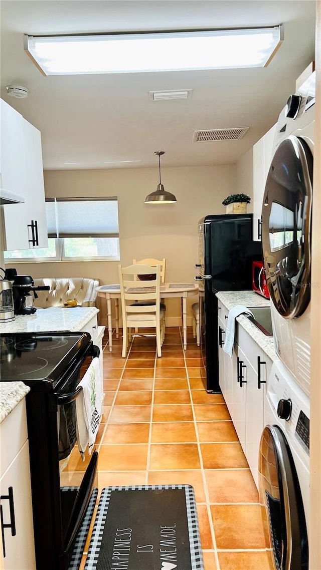 kitchen featuring white cabinetry, black appliances, stacked washer and clothes dryer, light tile patterned flooring, and pendant lighting