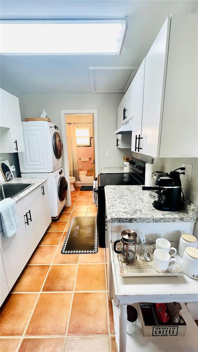 kitchen with light tile patterned floors, light stone counters, electric range, stacked washer / drying machine, and white cabinets