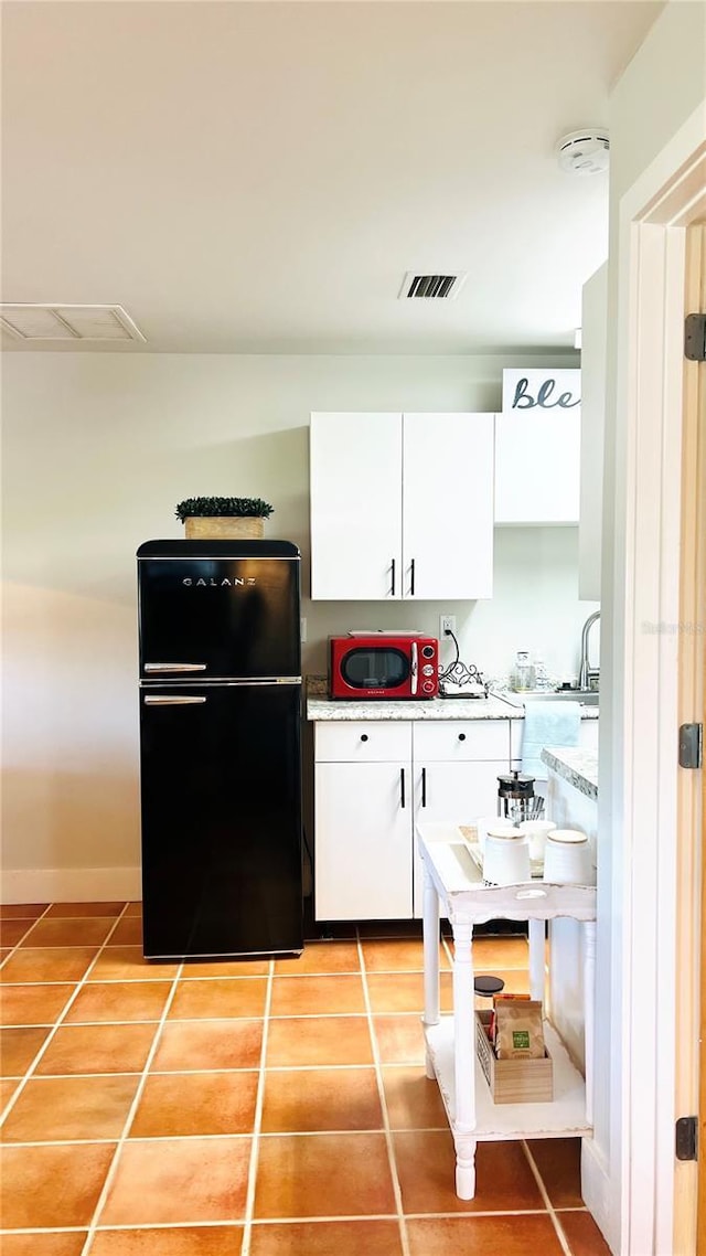 kitchen featuring light tile patterned flooring, white cabinetry, and black fridge